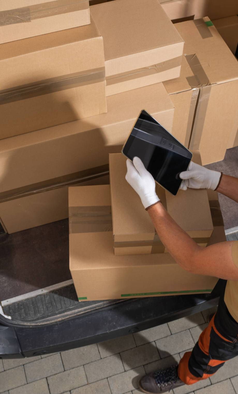 Courier is actively unloading shipping boxes from the back of a truck onto the ground.