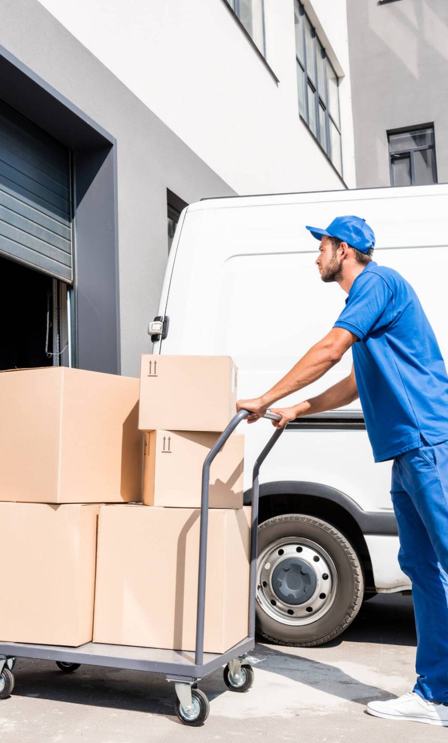 young delivery man with cardboard boxes on cart driving into warehouse